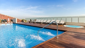 Una piscina en la azotea con terraza de madera, sillas de descanso y un jacuzzi.