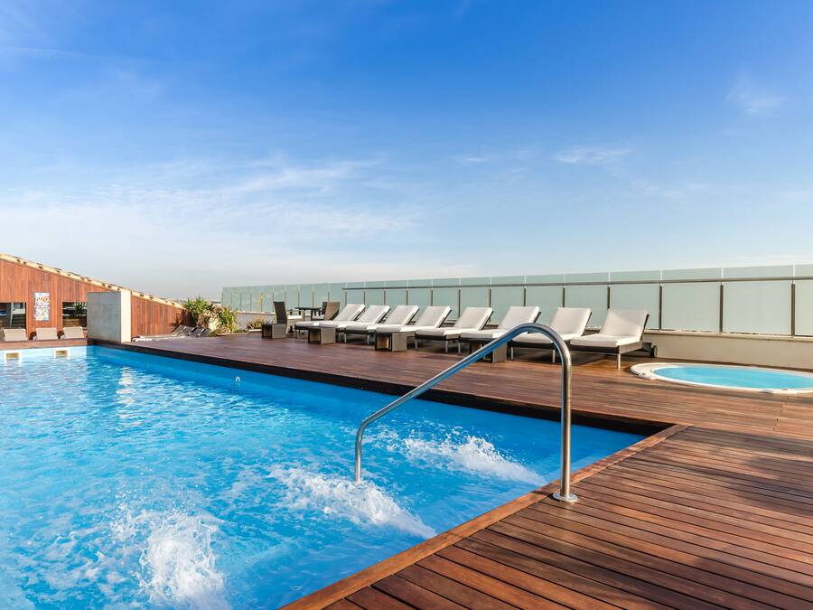 Una piscina en la azotea con terraza de madera, sillas de descanso y un jacuzzi.
