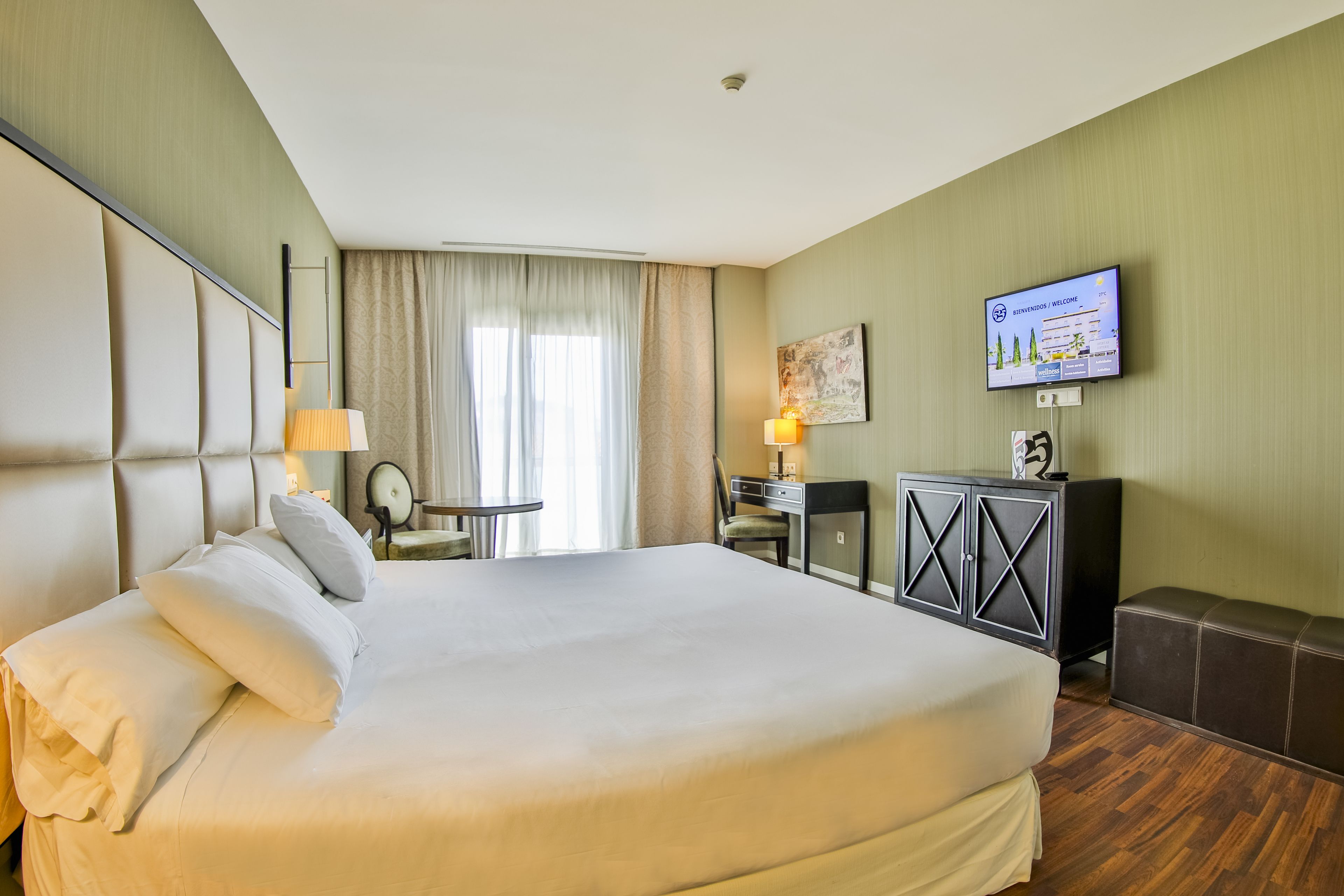 A hotel room with a large bed, a desk, a chair, a television, and a cabinet.