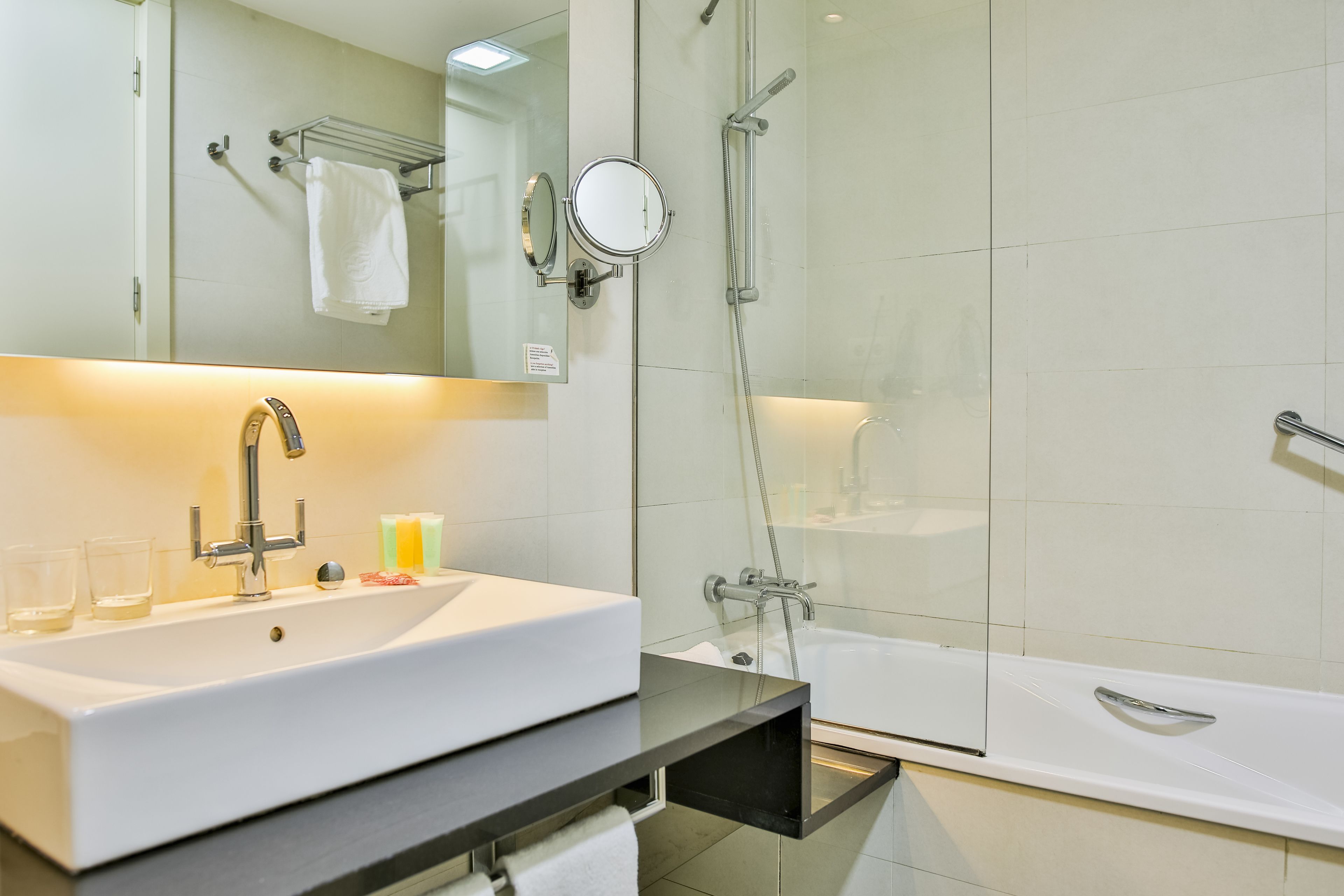 A modern bathroom with a white sink, a mirror, a glass shower enclosure, and a bathtub.
