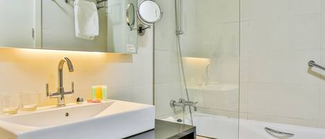 A modern bathroom with a white sink, a mirror, a glass shower enclosure, and a bathtub.