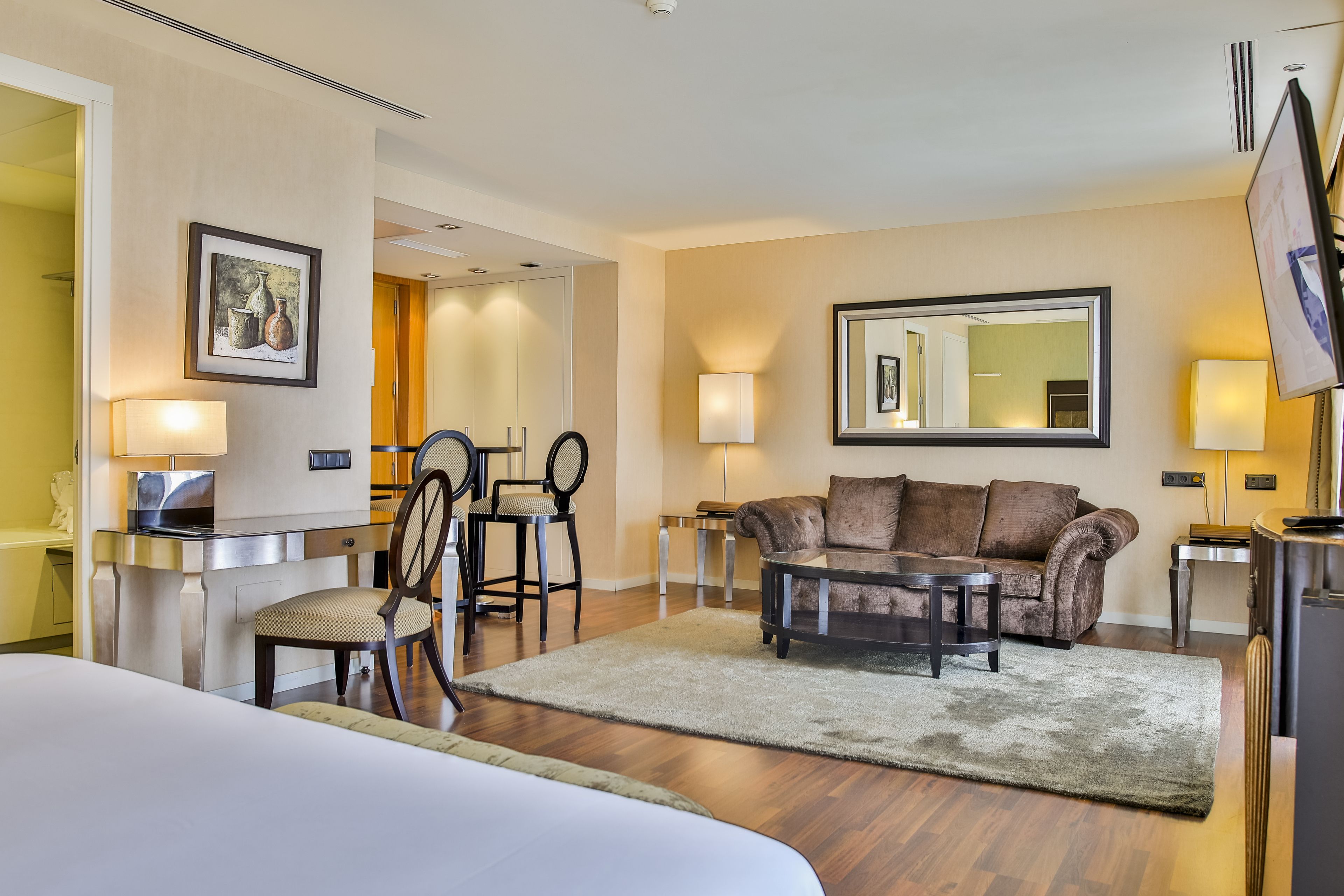 A hotel room with a bed, a sofa, a coffee table, a TV, a desk with a lamp, and a chair.
