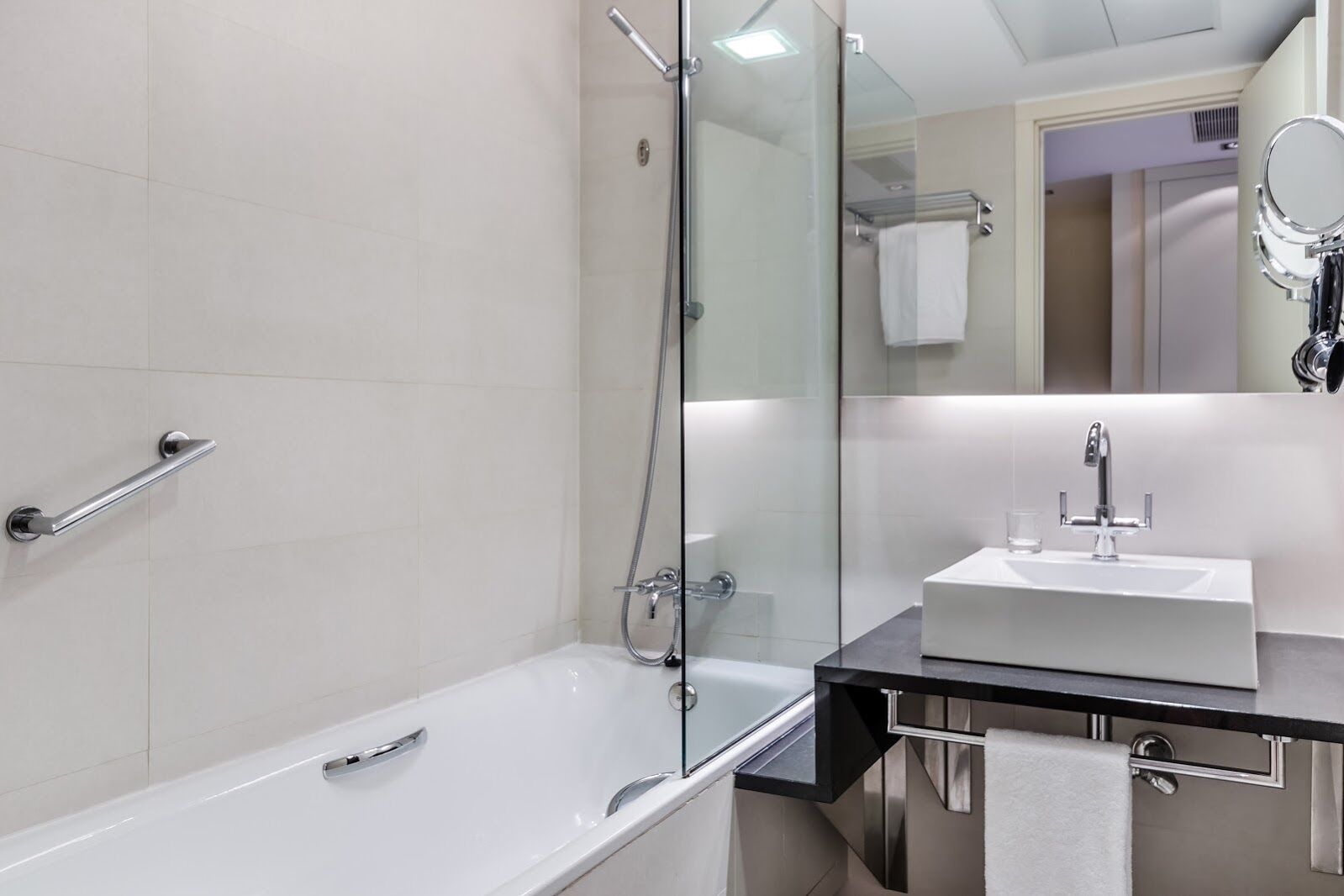 Une salle de bain moderne avec une douche à parois de verre, une baignoire blanche et un lavabo noir sur un plan de travail, avec un miroir au-dessus.