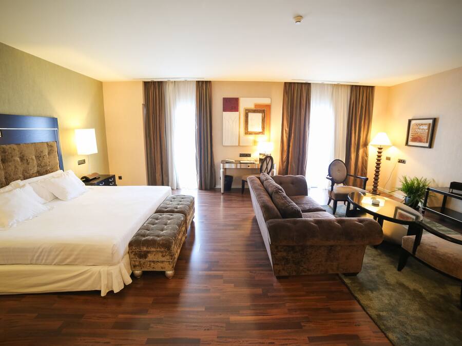 A hotel room with a large bed, a sofa, a desk, and a chair.