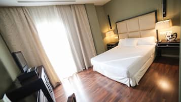 A hotel room with a large bed, two bedside tables with lamps, a desk with a chair, and a large window with curtains.