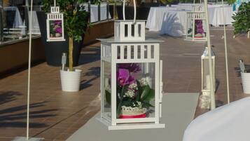 A rooftop terrace with white lanterns, potted plants, and tables set up for an event.