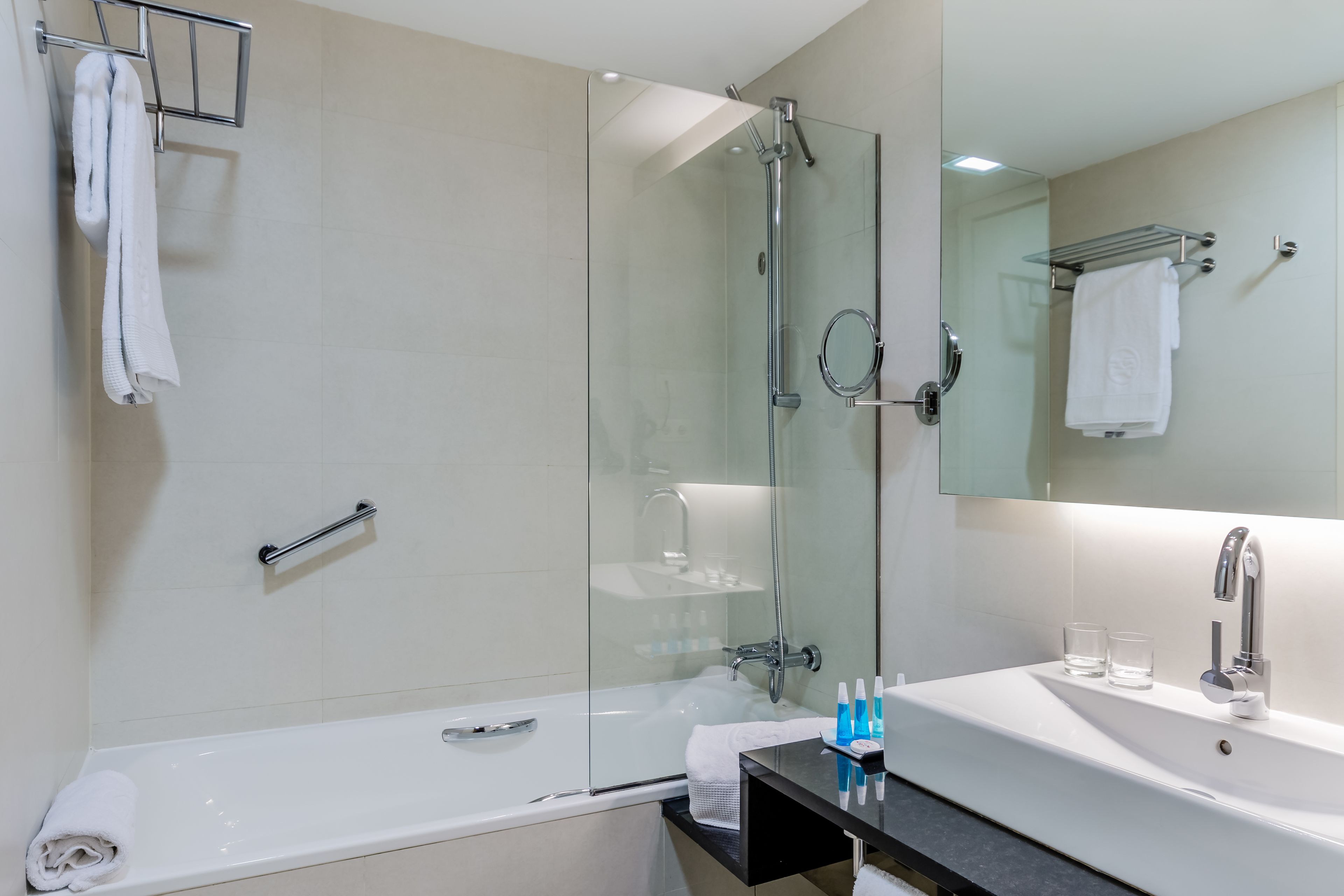 Een moderne badkamer met een douchecabine van glas, een witte badkuip, een wastafel met spiegel en een handdoekrek.