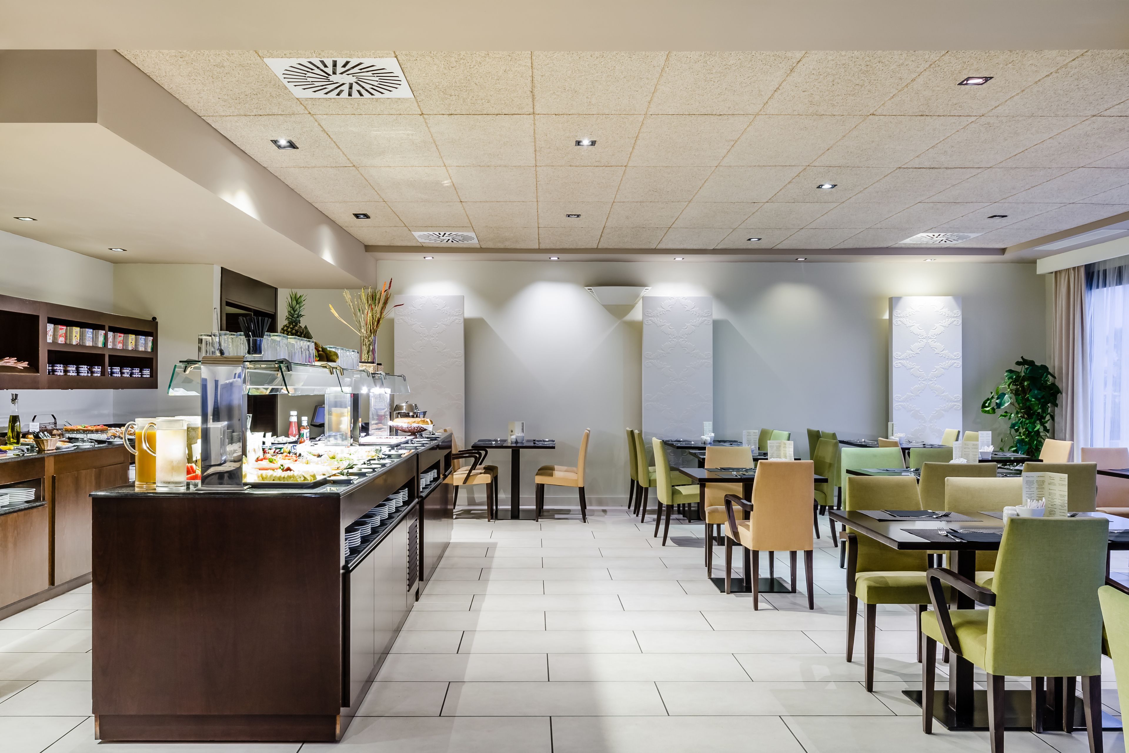 Un comedor amplio con varias mesas y sillas, una barra de buffet con diferentes alimentos, y un diseño interior moderno y elegante.