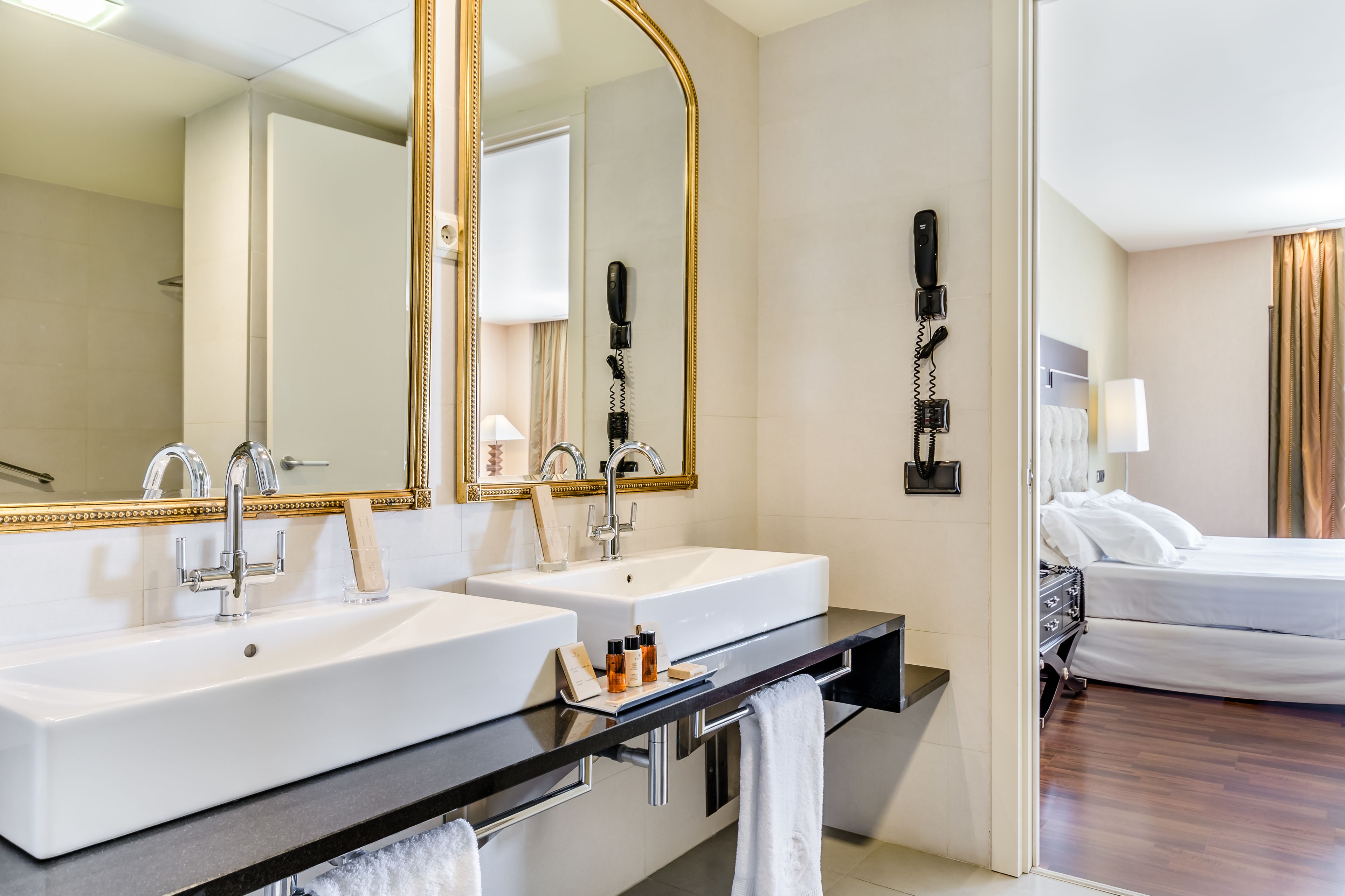 A hotel bathroom with two sinks, a large mirror, and a hairdryer on the wall.
