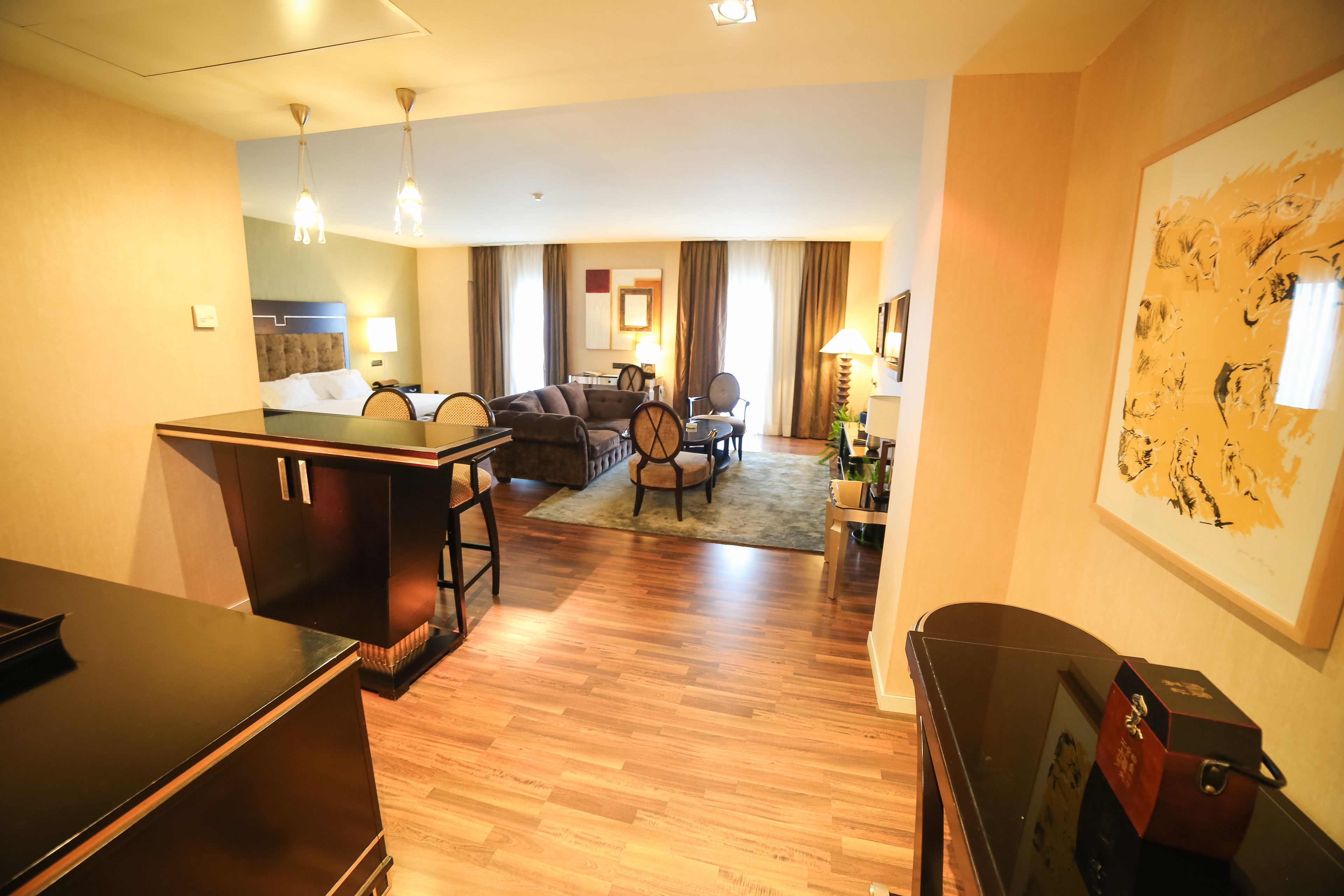 Habitación de hotel con piso de madera, un área de comedor con mesa y sillas, un sofá y un cuadro grande en la pared.