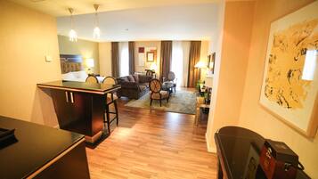A hotel room with a wooden floor, a dining area with a table and chairs, a sofa, and a large painting on the wall.