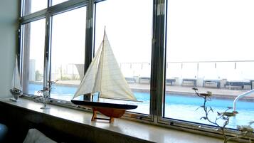 Una habitación con un ventanal grande que da a una piscina, un modelo de velero en el alféizar y una planta también allí.