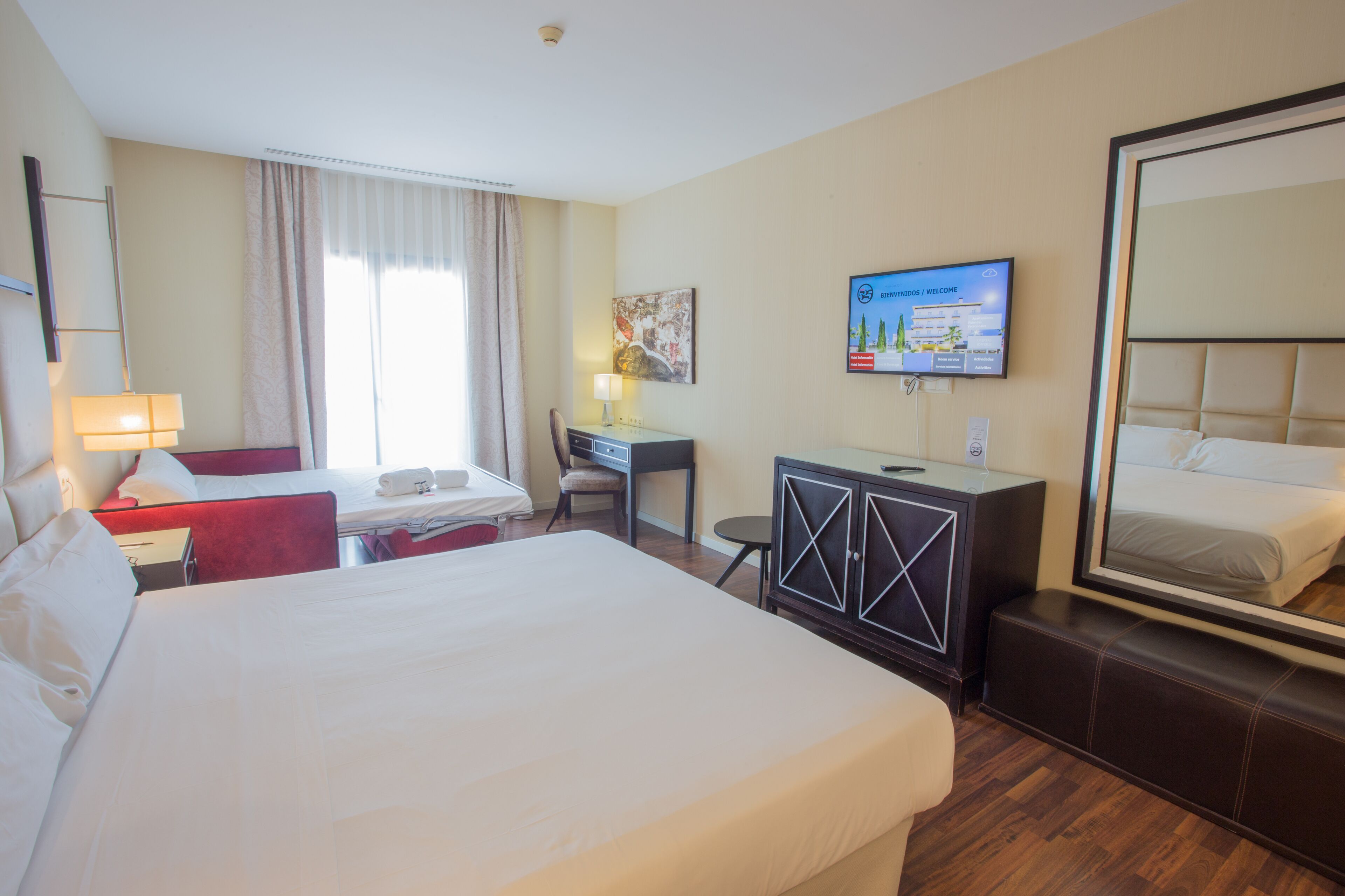Une chambre d’hôtel avec un grand lit, un bureau avec une chaise, une télévision et une armoire.