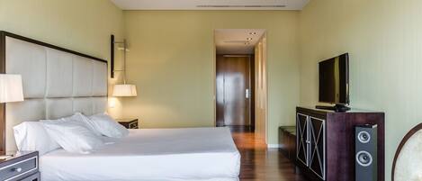 A hotel room with a large bed, a TV, a cabinet with speakers, and a hallway leading to another room.