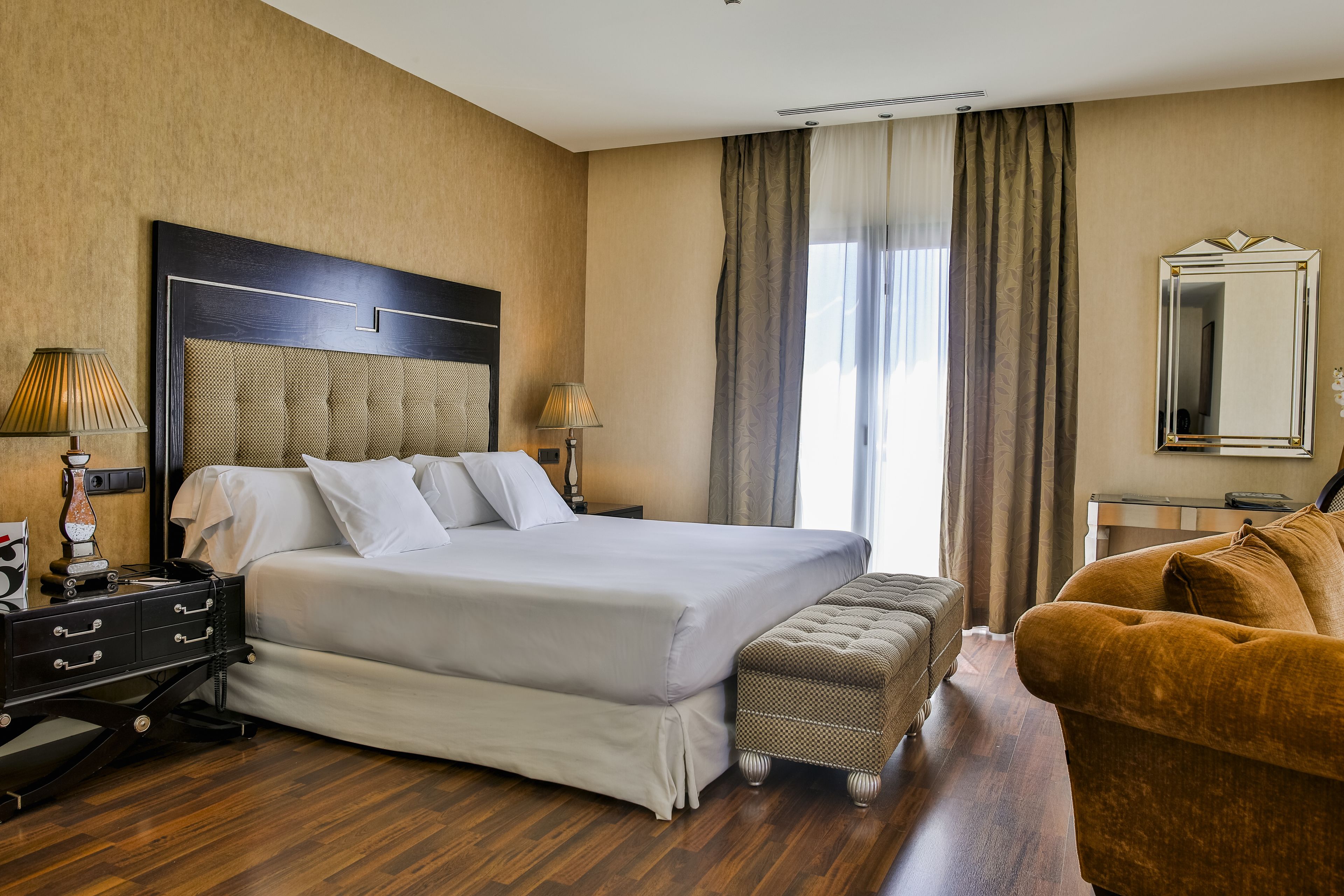 Une chambre d’hôtel avec un grand lit, un plancher en bois, un canapé, une table de chevet et un miroir.