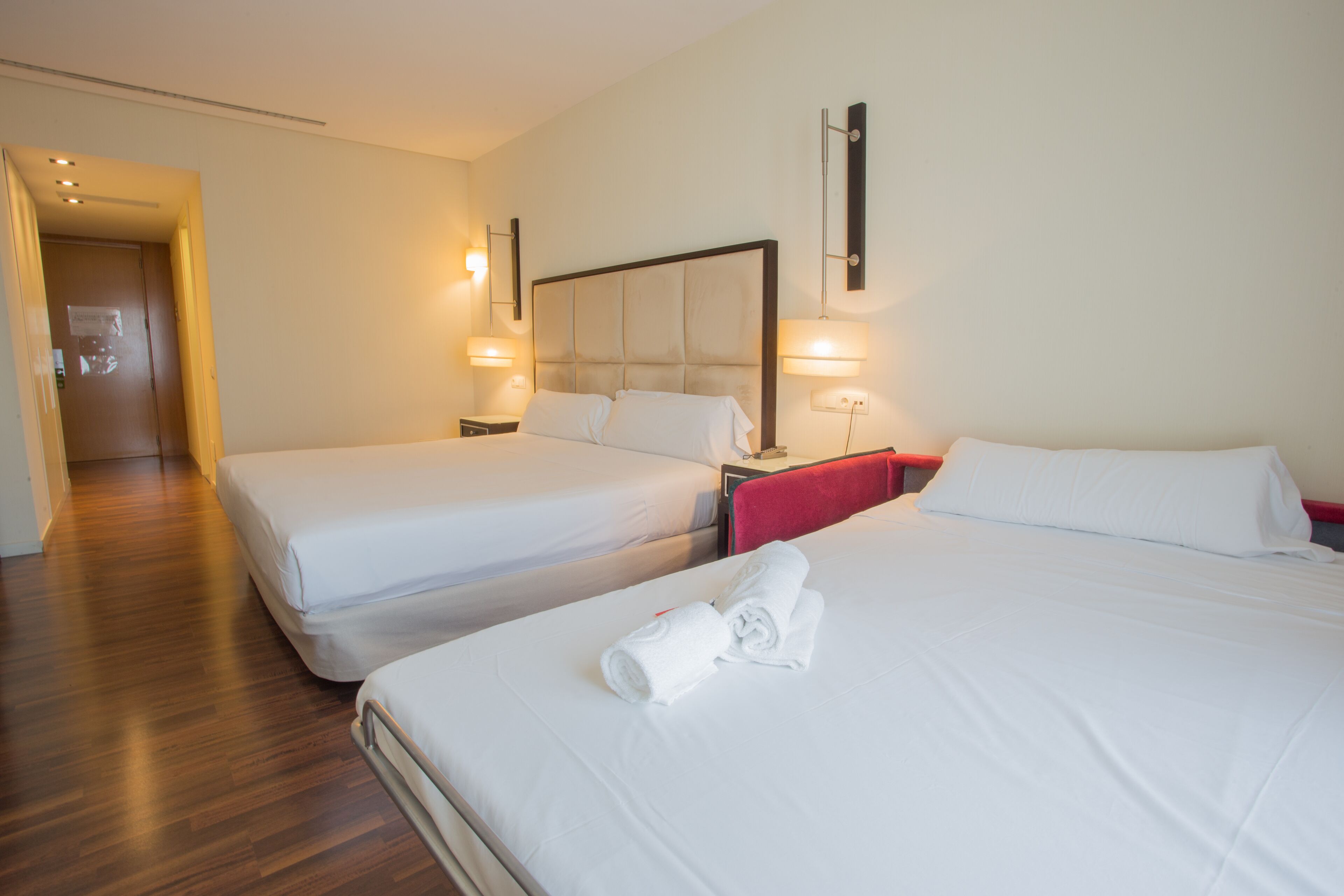 Two single beds with white linens, a wooden floor, and a red chair.