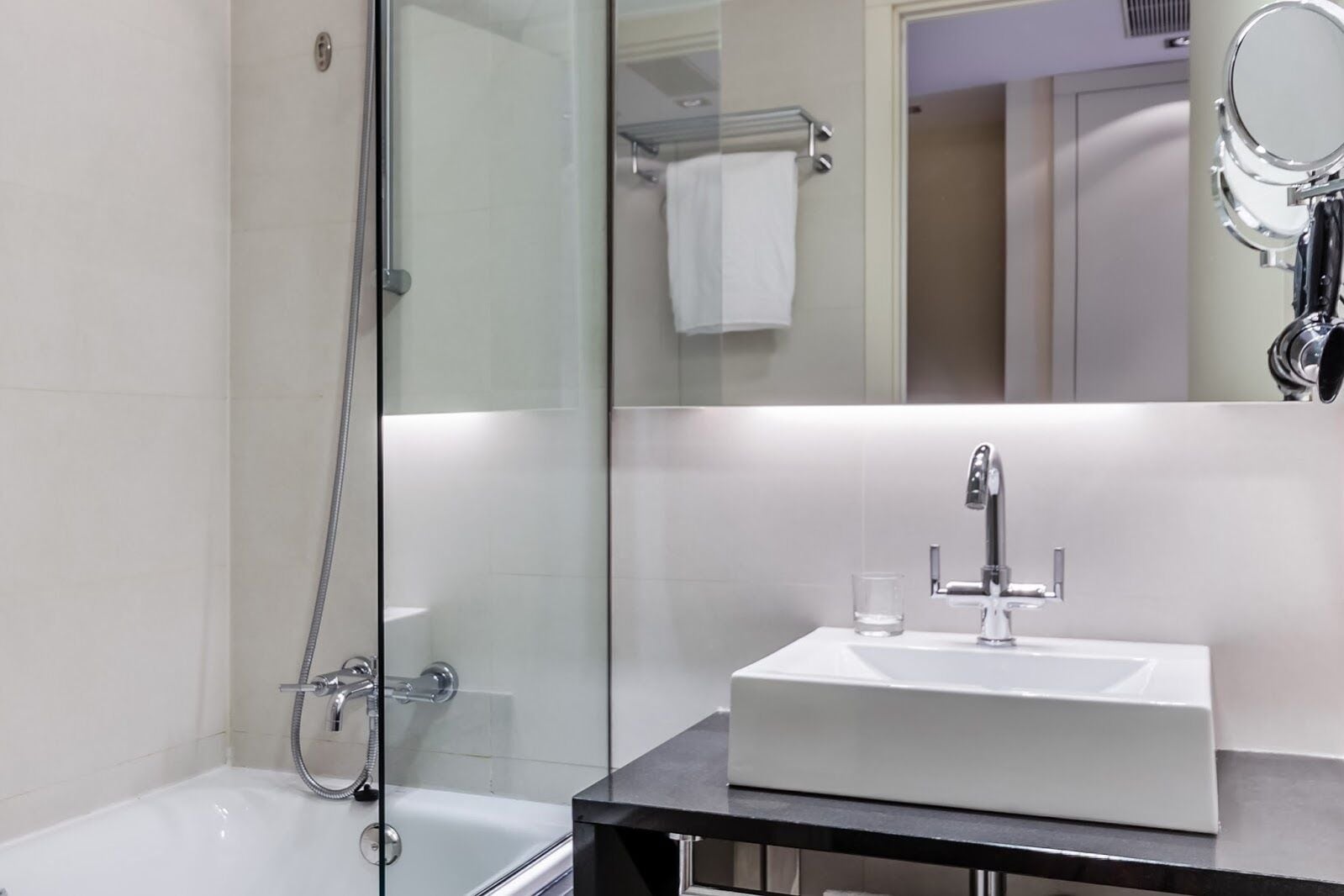 A modern bathroom with a glass-enclosed shower, a white sink with a mirror above it, and a towel rack in the background.
