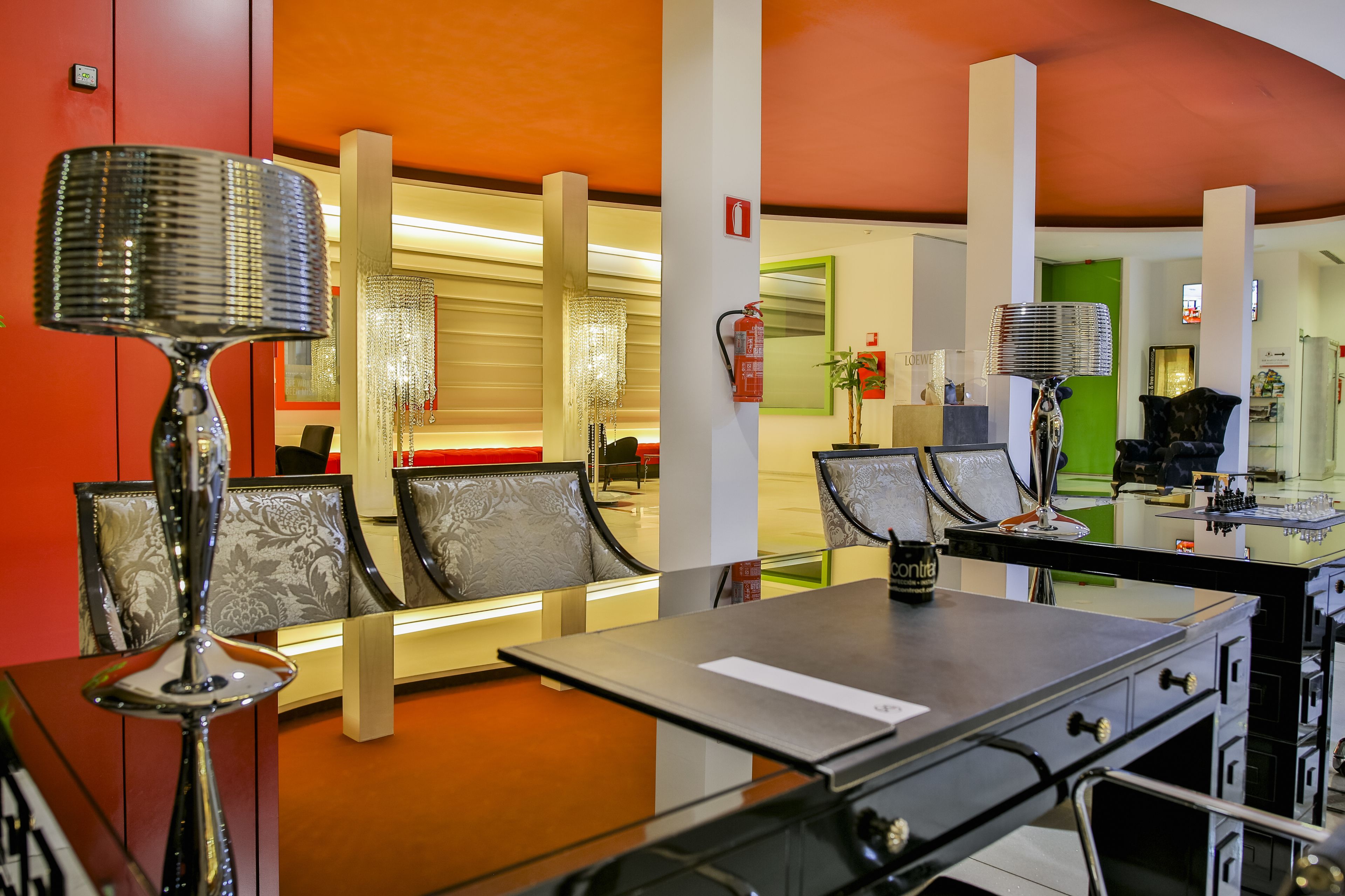 Eine moderne Hotelhalle mit Sitzgelegenheit, einer Rezeption und einem Feuerlöscher.