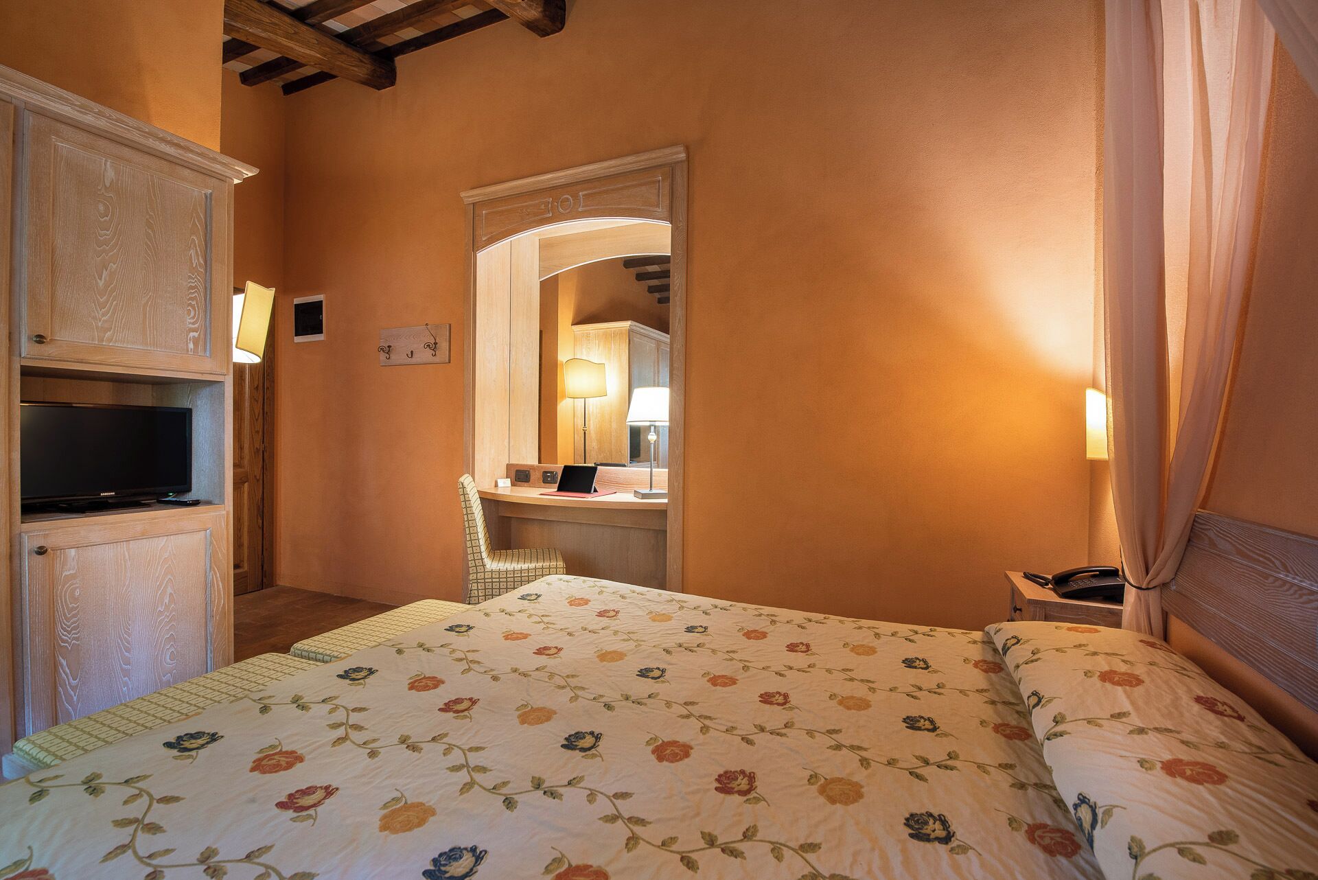 A hotel room with a bed, a television, a desk with a lamp, and a mirror.
