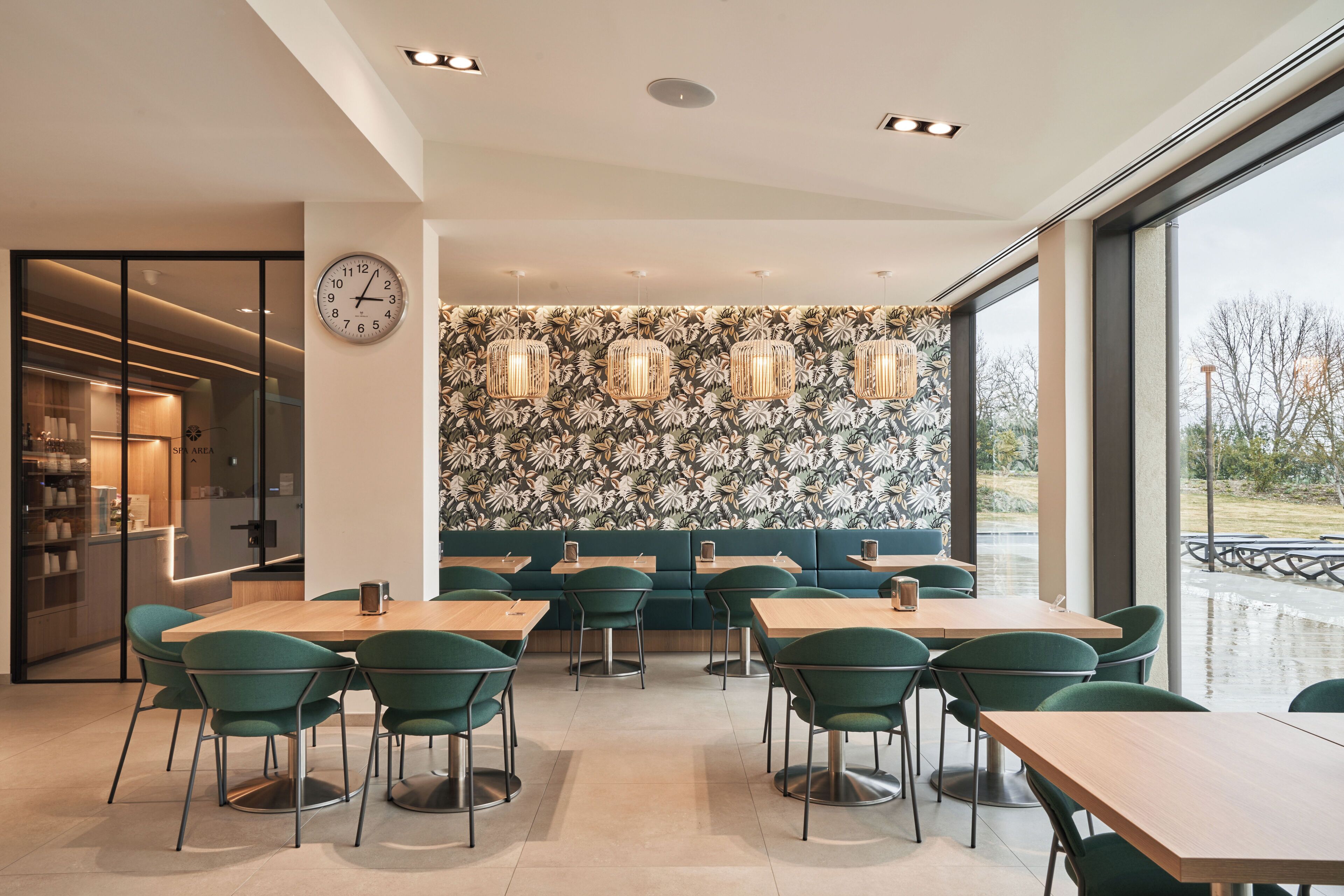 A modern dining area with green chairs and tables, a wall clock, and a patterned wallpaper.