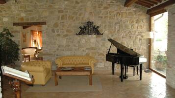 Una habitación con paredes de piedra, un piano, un sofá amarillo, una mesa de centro de madera y una lámpara.