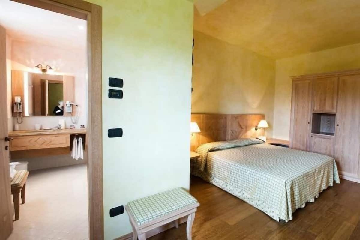 Een slaapkamer met een bed, nachtkastje, lamp en een kledingkast.