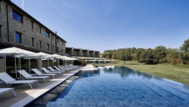 A poolside area with lounge chairs and umbrellas, a stone building, and a clear blue sky.