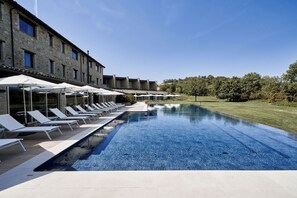A poolside area with lounge chairs and umbrellas, a stone building, and a clear blue sky. - Borgo Lanciano Resort & Spa (Castelraimondo)