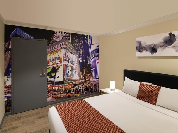 Habitación de hotel con un mural de gran tamaño que muestra un paisaje urbano, una cama con ropa de cama estampada, una mesita de noche con una lámpara y un cuadro sobre la cama.