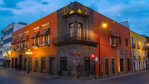 Un edificio histórico con una entrada destacada en esquina, grandes ventanales y un balcón.