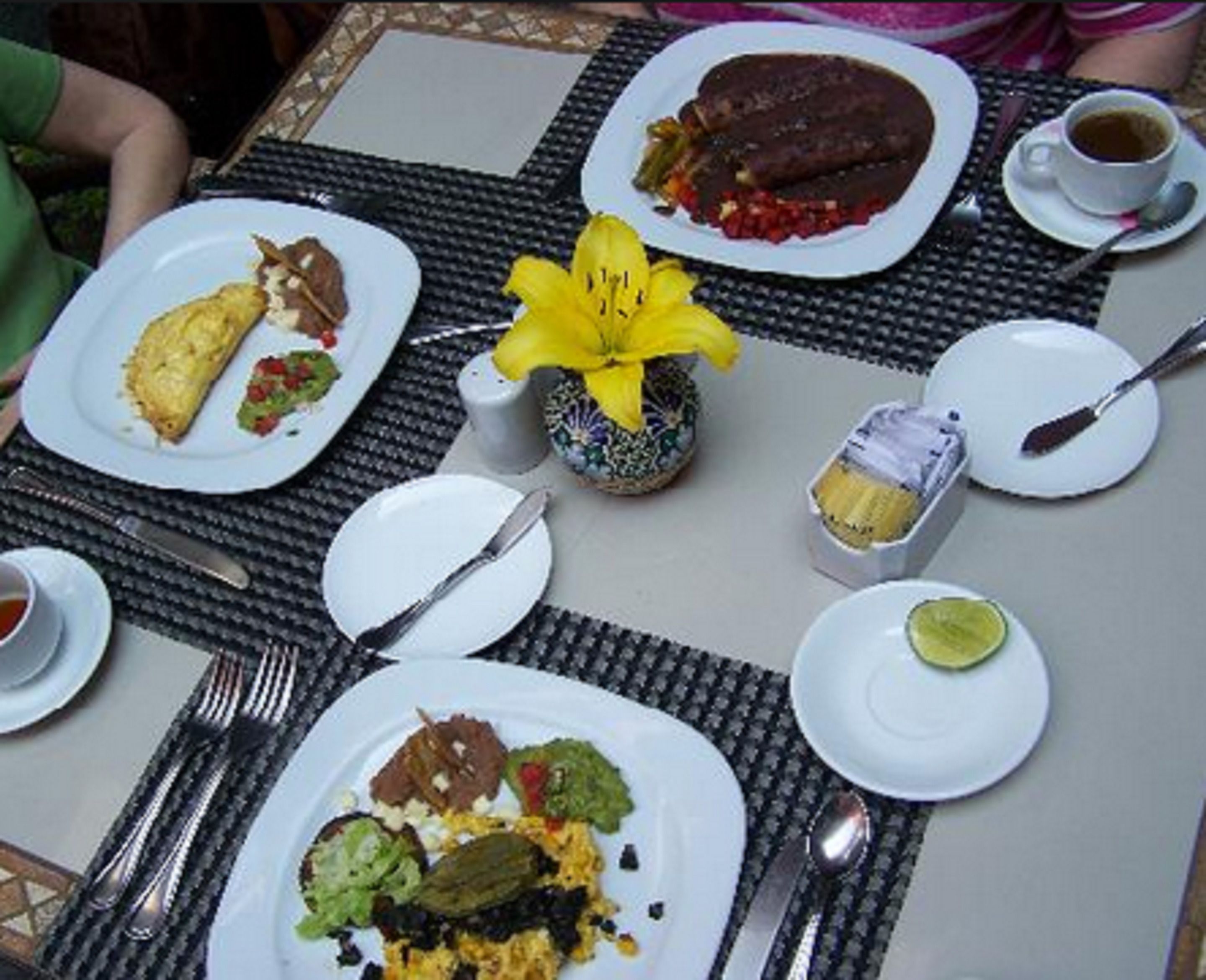 Una mesa dispuesta con platos de comida, utensilios y una pequeña flor amarilla.