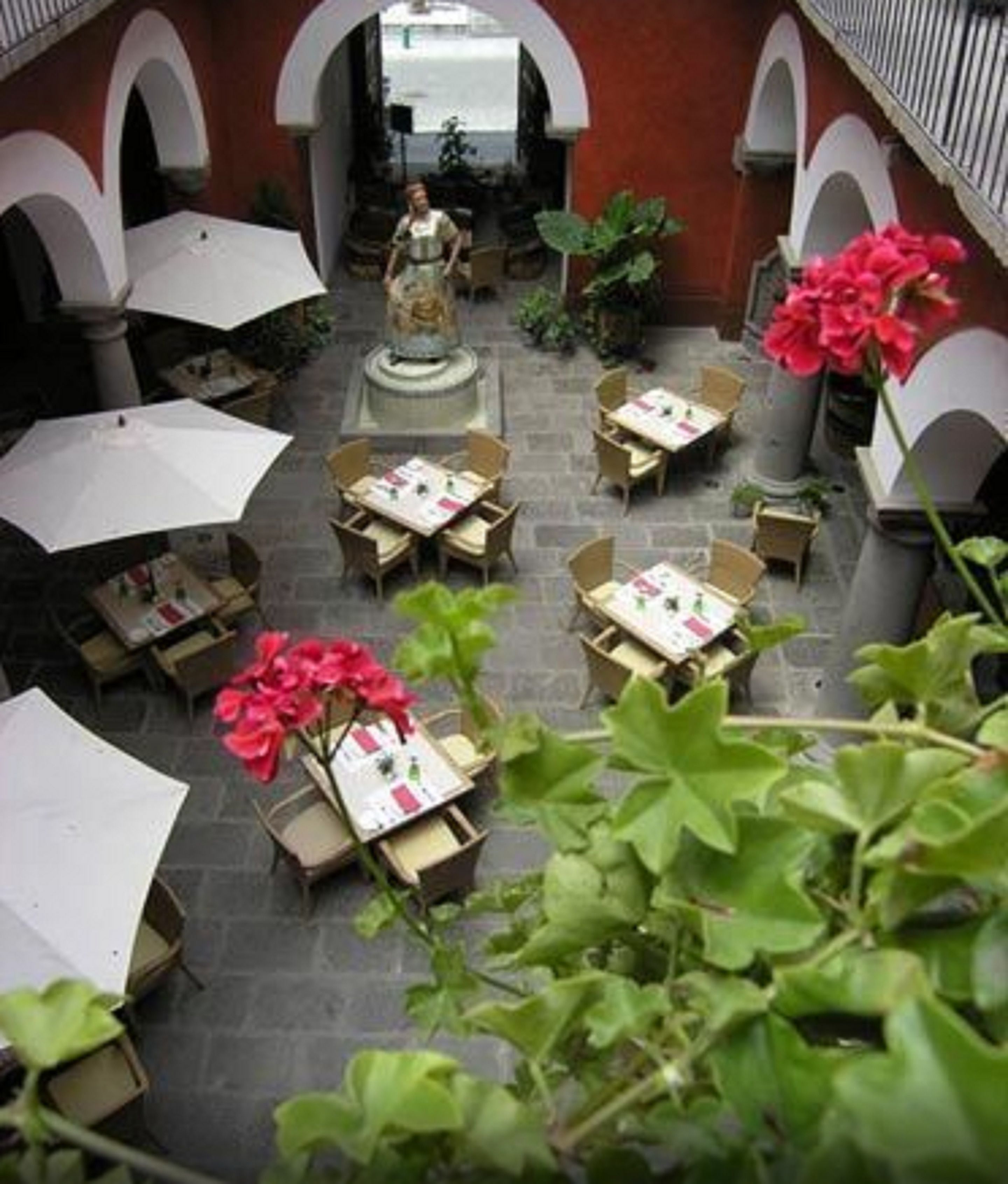 En udendørs café med borde og stole, omgivet af hvælvinger og plantekasser.