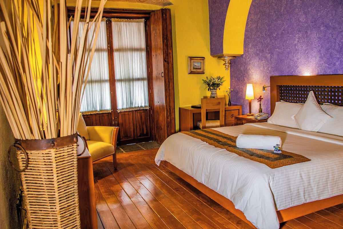 A hotel room with a wooden bed, a chair, a nightstand, and a window with curtains.