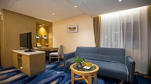 Habitación de hotel con sofá, una mesita con fruta, escritorio y computadora, y televisor.