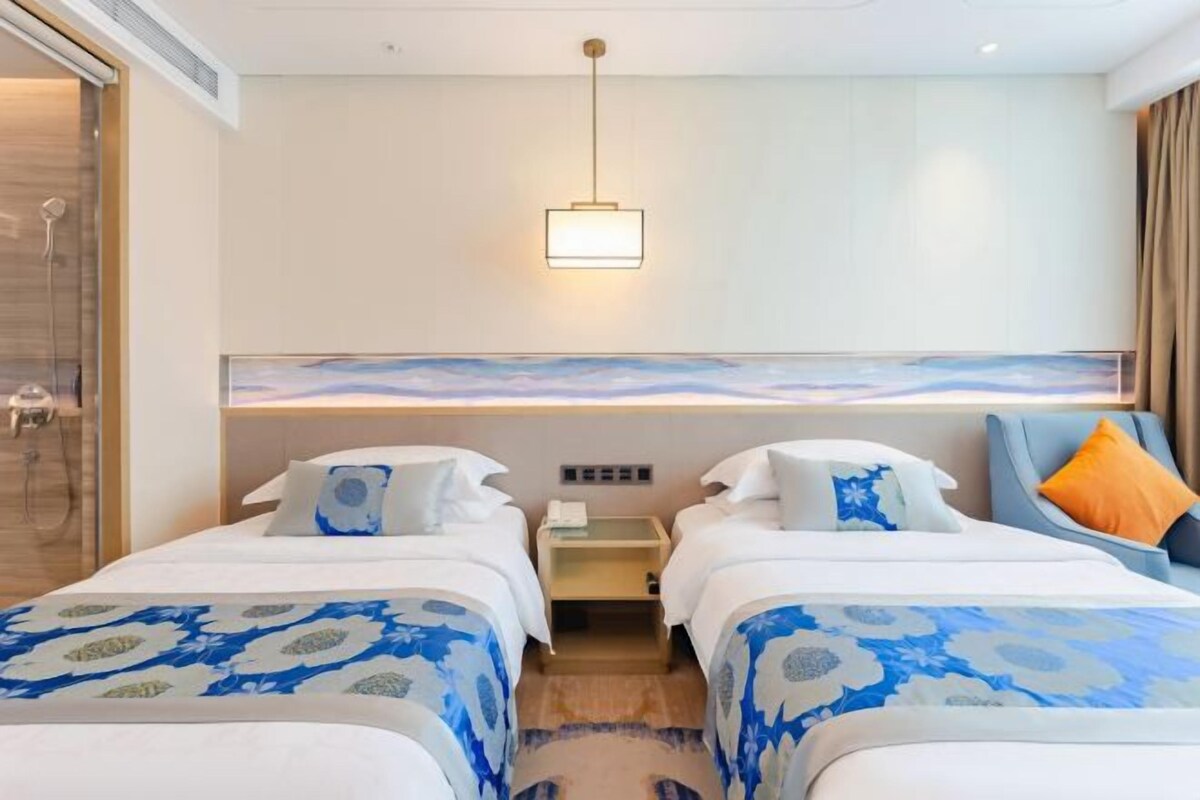Habitació d'hotel amb dos llits, una dutxa, una taula de nit i una làmpada de paret.