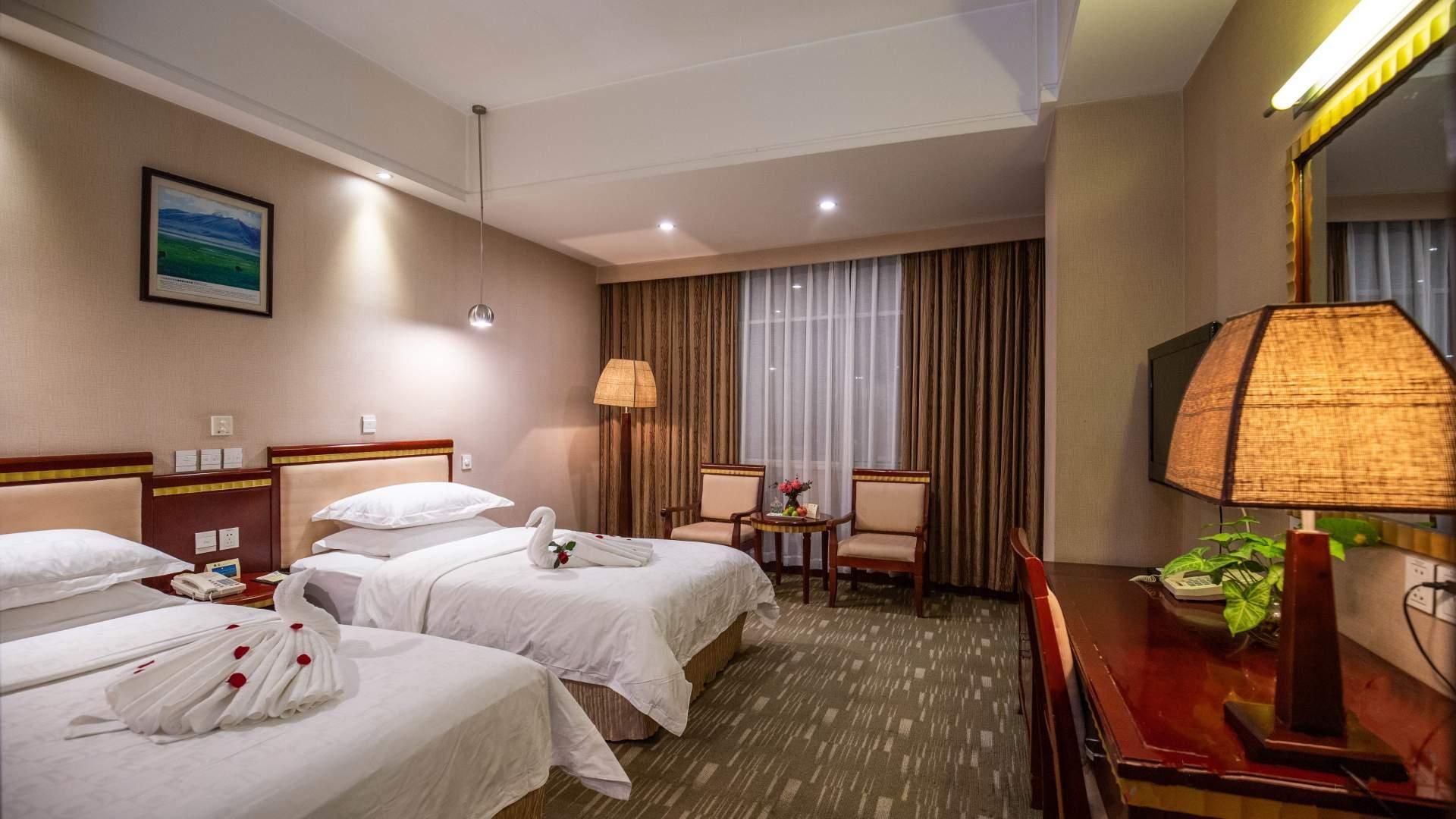 Une chambre d’hôtel avec deux lits, un bureau, une chaise, une lampe et un tableau au mur.