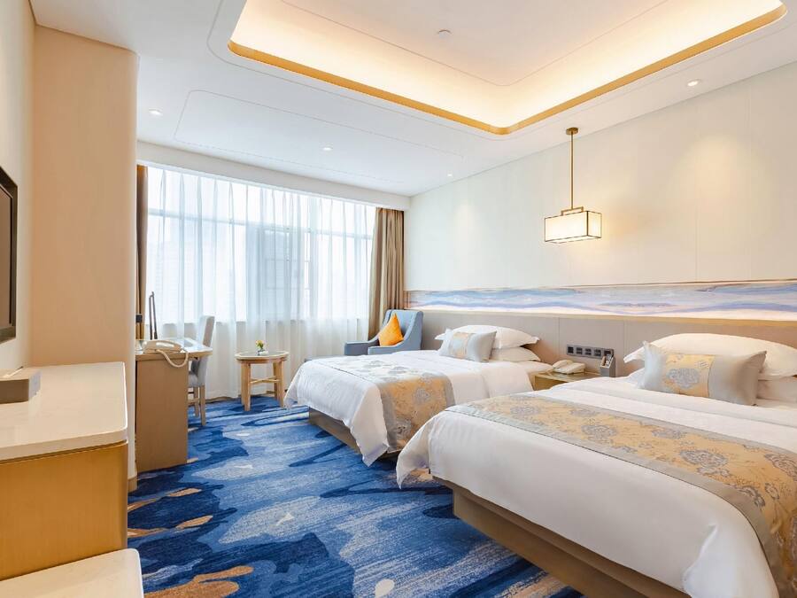 Une chambre d’hôtel avec deux lits, un bureau, une chaise et une grande fenêtre.