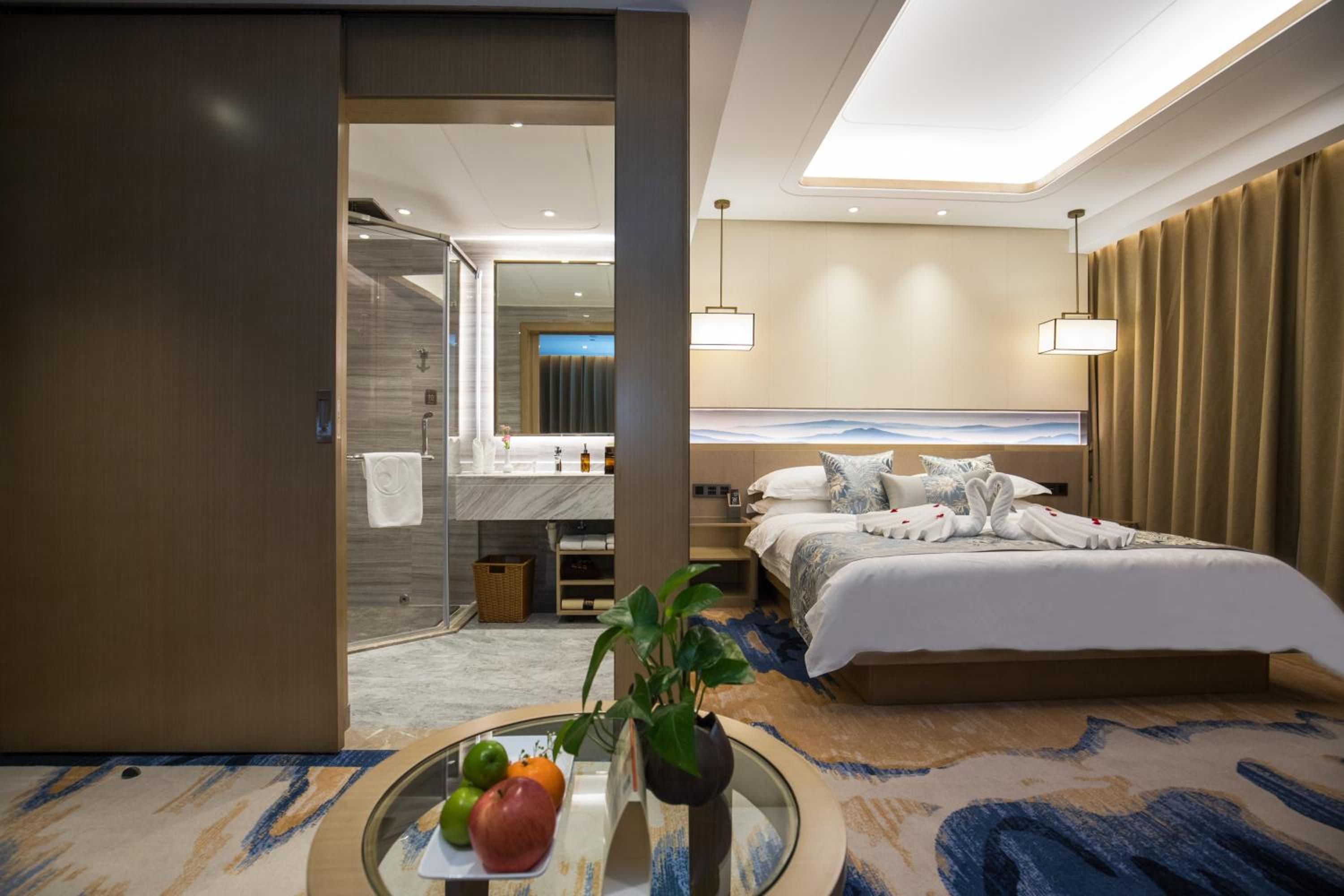 A hotel room with a bed, bedside table, and a bathroom with a shower and mirror.