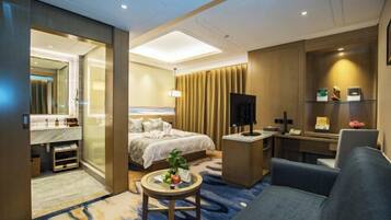 A hotel room with a bed, a desk, a chair, a small table with fruit, and a TV.