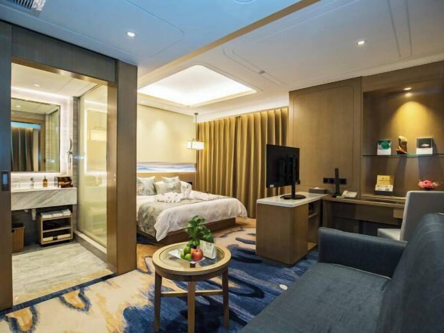 A hotel room with a bed, a desk, a chair, a small table with fruit, and a TV.