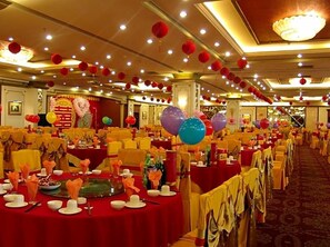 Un salón de banquetes con mesas redondas dispuestas para un evento formal, decorado con globos y centros de mesa.
