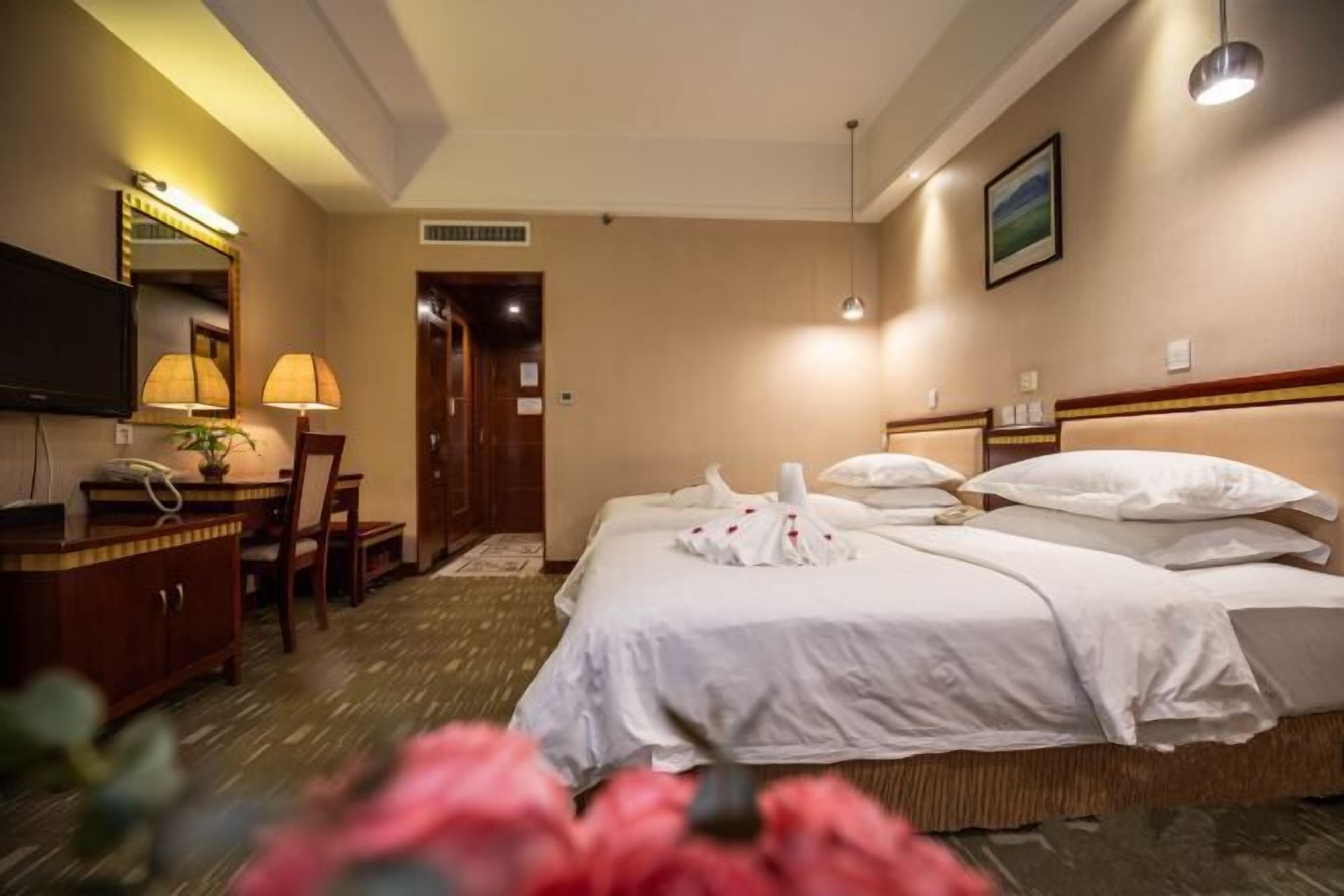 Een hotelkamer met een bed, een bureau met lamp, een stoel, een televisie en een lijst aan de muur.