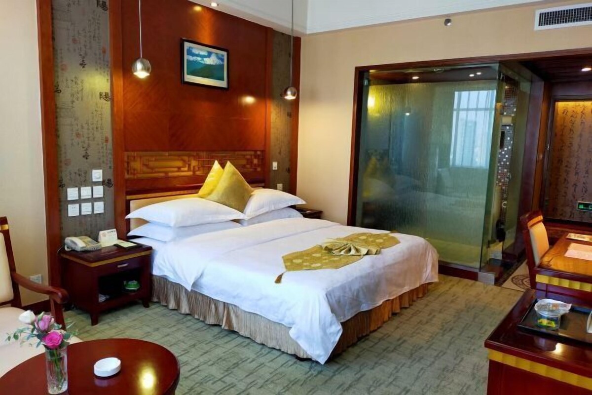 Habitación de hotel con una cama grande, un escritorio, una silla, una mesita y un florero con flores.