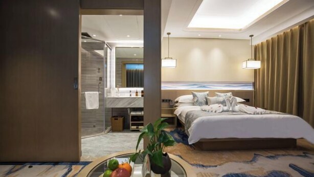 A modern hotel room with a large bed, a bathroom with a shower, and a dining area with a table and chairs. - Golden Spring Hotel (Kunming)