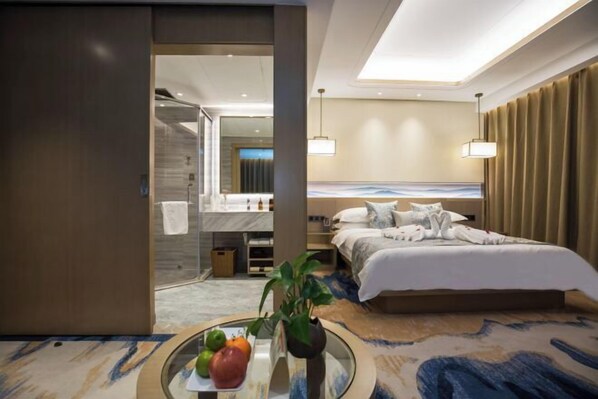Una habitación de hotel moderna con una cama grande, un baño con ducha y un área de comedor con mesa y sillas.