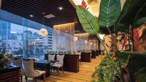 A modern indoor space with a wooden floor, seating area, and large windows offering a city view.