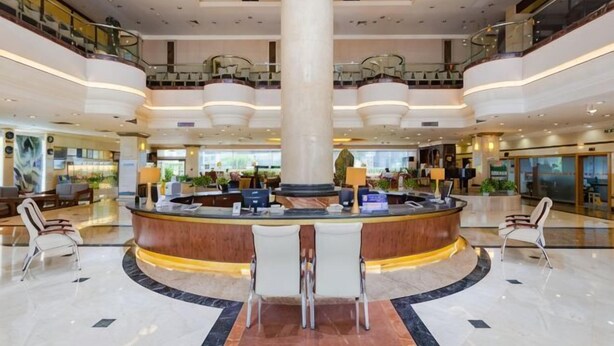 A spacious lobby with a central reception desk, multiple seating areas, and a high ceiling with a large column.