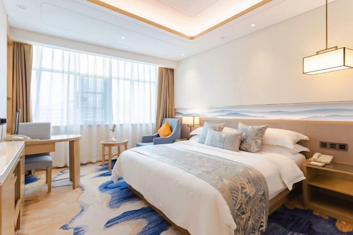 Habitación de hotel con una cama grande, un escritorio, una silla y vistas al mar a través de la ventana.