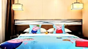 A hotel room with a bed featuring cartoon character pillows, a blue bedspread with similar characters, and a modern headboard. - Golden Spring Hotel (Kunming)