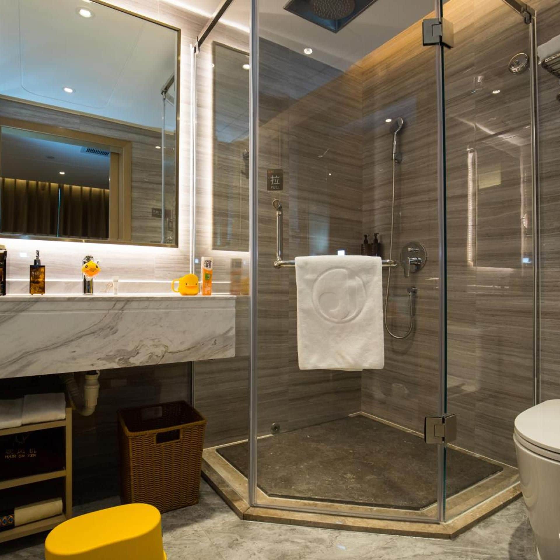 A modern bathroom with a glass-enclosed shower, a marble countertop, and a visible towel rack.